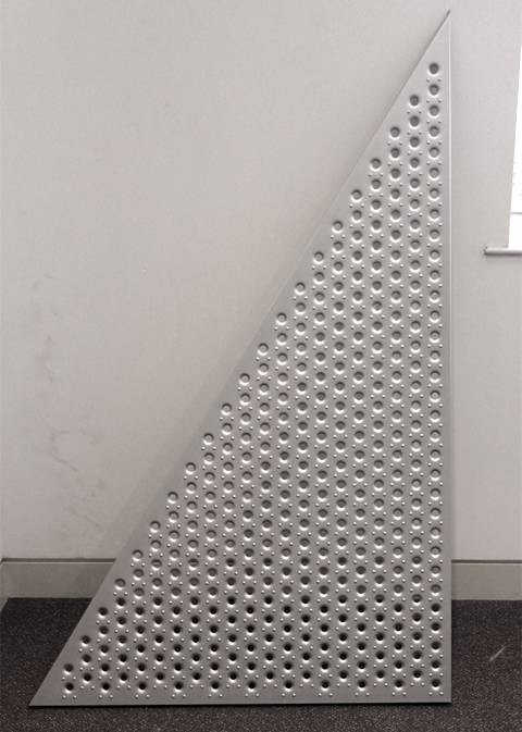 A piece of triangle embossed sheet with round holes is against a wall.